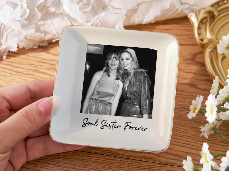 May include: Square, off-white ceramic trinket dish with a gold rim, featuring a black and white photo of two women. The words "Soul Sister Forever" are written below the photo in a script font.