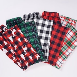 May include: Six pairs of red and green plaid pyjama trousers with different patterns. The trousers are folded and arranged in a fan shape.