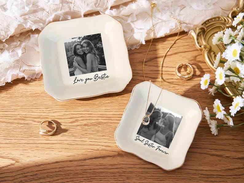 May include: Two off-white ceramic trinket dishes with gold trim, each featuring a black and white photo. One says "Love you Bestie," the other "Soul Sister Forever." Gold jewelry and a ring are also present.
