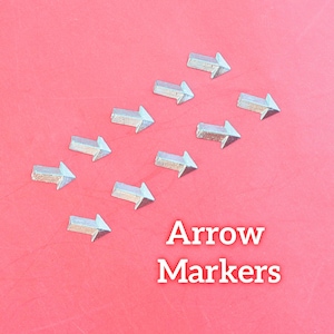 May include: Arrangement of silver arrow markers on a red background. The text "Arrow Markers" is displayed in white. The arrows are pointing to the right.