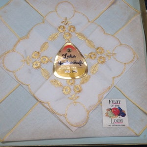 May include: A set of two white handkerchiefs with gold embroidered floral designs, presented in a box. The handkerchiefs feature intricate gold detailing and are labeled "Ladies Handkerchiefs". A small tag reads "Fruit of the Loom".