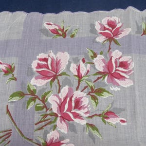 May include: A sheer white handkerchief featuring a scalloped edge and a light purple plaid pattern. The fabric is decorated with a floral print of pink roses, rosebuds, and green leaves arranged in a cluster across the corner of the square cloth.