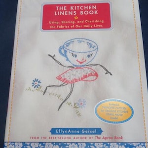 May include: The Kitchen Linens Book by EllynAnne Geisel, a book about using, sharing, and cherishing the fabrics of our daily lives. The cover features a whimsical illustration of a teacup with a face and a skirt, embroidered on a white background.