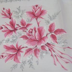 May include: A white fabric handkerchief featuring a central floral print of pink roses with white highlights and delicate grey line-drawn leaves. The design includes a thin grey decorative border along the top edge of the square textile piece.