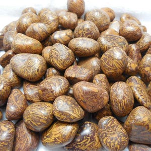 May include: A pile of polished, oval-shaped stones. The stones are primarily brown with intricate yellow and tan veining patterns. The smooth, rounded stones vary in size and are arranged closely together.