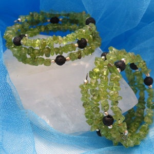 May include: Two green gemstone bracelets with black lava beads. The bracelets are wrapped around a white surface.