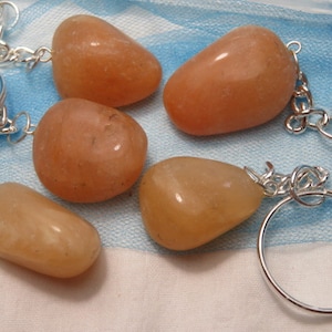 May include: Five smooth, light orange, natural stone keychains with silver key rings. The stones are attached to the rings with silver wire.