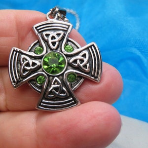 May include: Silver Celtic cross pendant with green crystal accents. The cross features a knot design and is a popular Irish symbol.