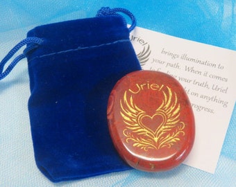May include: A red, oval-shaped stone with gold-colored wings and heart design, the name "Uriel" is above the design. A blue velvet drawstring bag is to the left. A white card with text is to the right.