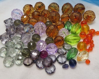 May include: Assortment of colorful glass beads in various shapes and sizes. The beads are in shades of purple, green, orange, and brown. Some beads are round, while others are faceted or oval.
