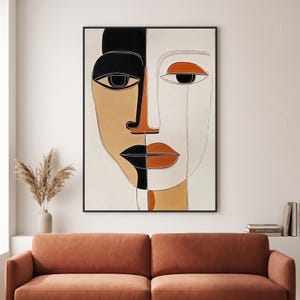 May include: A rectangular wall art print featuring a stylised, split-face portrait. The left side is rendered in black and tan, while the right side is in white and terracotta. The image uses bold black outlines to define the facial features.