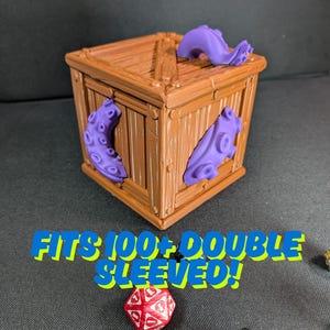 Peut inclure: Une boîte en bois marron avec des tentacules violets. Le texte "FITS 100+ DOUBLE SLEEVED!" en bleu et jaune est sur la boîte. Un dé rouge et blanc est devant la boîte. Rangement de dés.