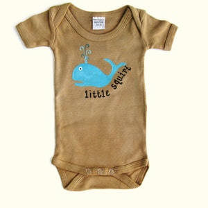 May include: A brown baby onesie with a blue whale graphic and the text "little squirt" printed on the front.