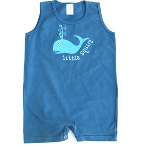 May include: A blue sleeveless onesie with a blue whale graphic and the text "little squirt" on the front.