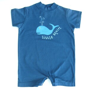 May include: A blue baby onesie with a white whale graphic and the text "little squirt" printed on the front.