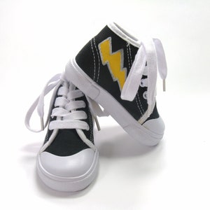 May include: A pair of black canvas high-top sneakers with white laces and a yellow lightning bolt design on one shoe.