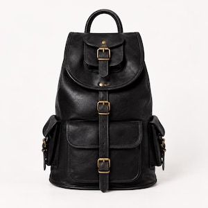 May include: A black backpack featuring a top handle, a fold-over flap with a buckle closure, and a front pocket with a vertical strap. The bag includes two side pockets and antique brass-toned metal hardware accents throughout the design.