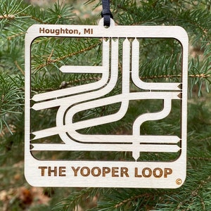 May include: A white wooden ornament shaped like the "Yooper Loop" in Houghton, Michigan. The ornament has a black string for hanging and the text "THE YOOPER LOOP" is printed on the bottom.