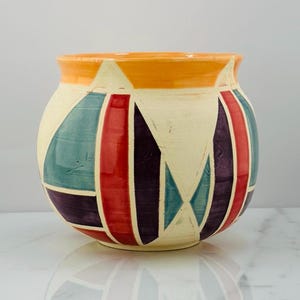 May include: A round ceramic vase with a geometric pattern in shades of orange, red, purple, teal, and white.
