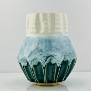 May include: A ceramic vase with a white rim and a blue and green glaze. The vase has a unique, textured design.