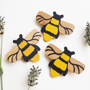 May include: Three wooden bee brooches painted in yellow and black. The bees are stylized and have a simple design.