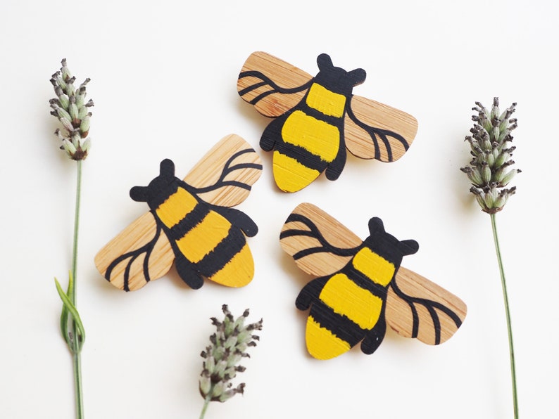 May include: Three wooden bee brooches painted in yellow and black. The bees are stylized and have a simple design.