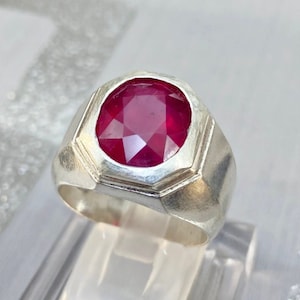 Könnte beinhalten: Ein silberner Ring mit einem großen, roten, facettierten Edelstein, der in einer Zargenfassung sitzt.