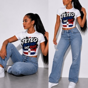 May include: A white short-sleeved crop top featuring a graphic print with the text "TETEO SPEND DAT $HIT" in black, blue, and red lettering, layered over a stylized Dominican Republic flag design with black paint splatter accents.