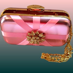 Precioso bolso de mano rosa metálico con cierre dorado y una delicada asa. Incluye cadena adjunta. Combina a la perfección con cualquier atuendo, tanto formal como informal.