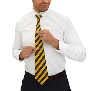 May include: A yellow and black striped tie with a repeating pattern of a dark design. The tie is being adjusted by a person wearing a white dress shirt and black pants.
