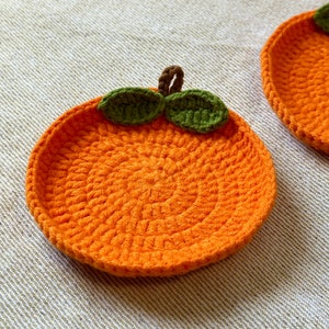 May include: Orange crochet coaster with green leaves. The coaster is round and has a textured surface.
