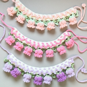 May include: Three crocheted necklaces featuring delicate flower embellishments. The necklaces are white with pink, light pink, and purple flowers.