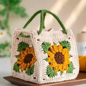 May include: A crocheted tote bag with a sunflower design. The bag is made with beige, green, and yellow yarn. The bag has two handles.