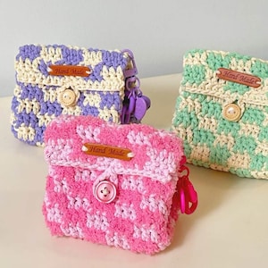May include: Three handmade crochet pouches in purple, pink, and green. Each pouch features a button closure and a small leather tag that reads "Hand Made". The pouches are designed with a checkered pattern and include a keychain.