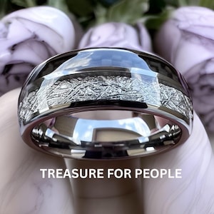 Könnte beinhalten: Nahaufnahme eines silbernen Rings mit poliertem Band und strukturiertem, gemustertem Mittelteil. Der Ring reflektiert den Himmel und die Umgebung. Der Text "TREASURE FOR PEOPLE" befindet sich am unteren Bildrand. Der Ring ist wahrscheinlich ein Schmuckstück.
