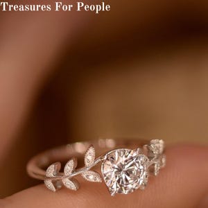 Puede incluir: Un anillo de plata con una gran piedra redonda transparente. La banda del anillo está decorada con un delicado diseño de hojas.