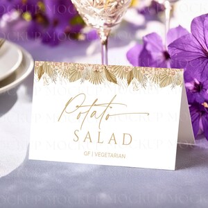May include: A white folded card with gold text that reads "Potato Salad". The card has a decorative border of dried flowers and foliage. The bottom of the card reads "GF | Vegetarian".