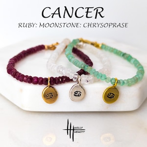 May include: Three gemstone bracelets with gold-colored charms featuring the Cancer zodiac symbol. The bracelets are made of ruby, moonstone, and chrysoprase beads. The word "CANCER" is written above the bracelets.