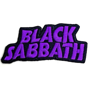 Puede incluir: Un parche de tela con el texto BLACK SABBATH bordado en hilo de color morado brillante. Las letras son gruesas y estilizadas, delineadas con un borde negro grueso que sigue el contorno de las palabras, creando un aspecto bicolor definido.