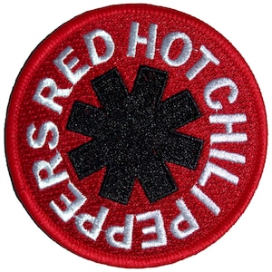 May include: A circular patch with a red background and white embroidered text that reads "RED HOT CHILI PEPPERS". A black asterisk-like symbol is in the center. The patch has a stitched border.