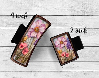 May include: Two black hair clips with floral designs. One clip is 4 inches long, the other is 2 inches long. The floral designs feature pink and purple flowers with a vintage paper background.