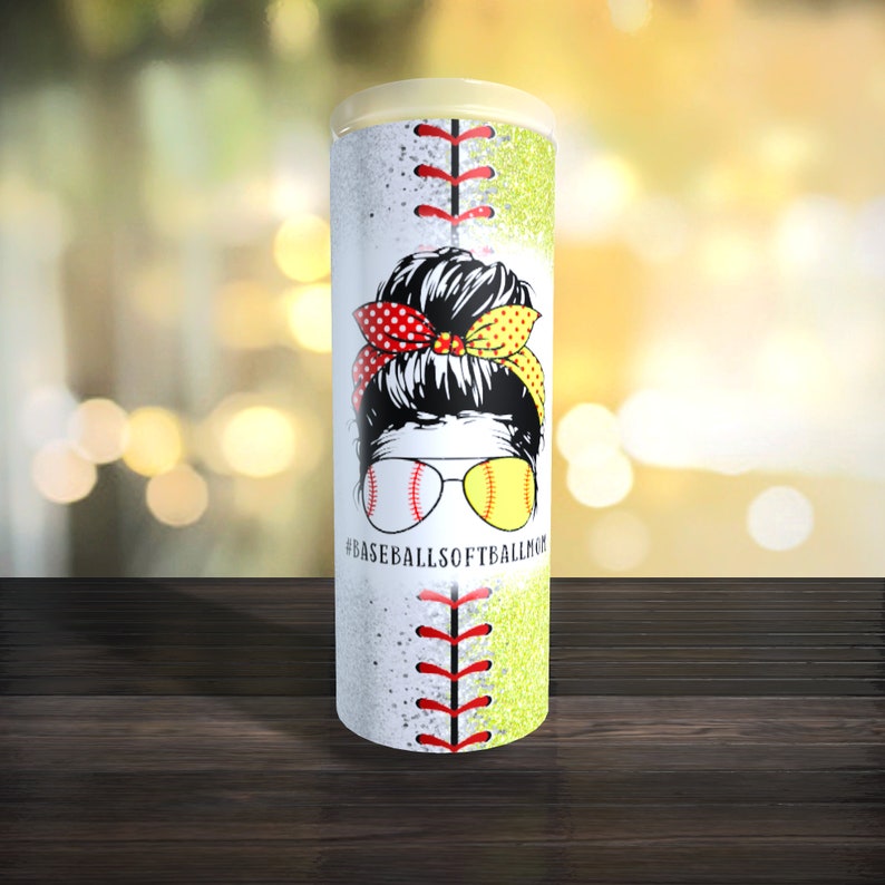 May include: A white and yellow tumbler with a baseball and softball design. The tumbler features a woman with a messy bun and sunglasses. The text "#BASEBALLSOFTBALLMOM" is printed on the tumbler.