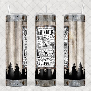 May include: A stainless steel tumbler with a wooden plank design and the words "Cabin Rules" in a rectangular frame. The tumbler has a black forest silhouette at the bottom and a silver lid with a straw.