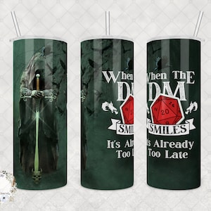 May include: A green and black tumbler with a design of a hooded figure holding a sword. The other side of the tumbler has a red 20-sided die with the text "When the DM Smiles It's Already Too Late".
