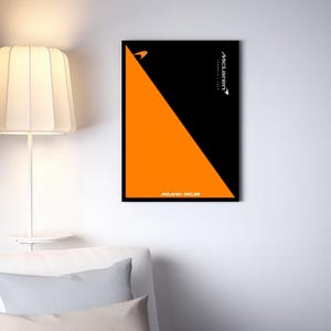 May include: A framed poster with a black and orange geometric design. The poster features a diagonal orange triangle against a black background. The McLaren Formula 1 Team logo and text are visible.