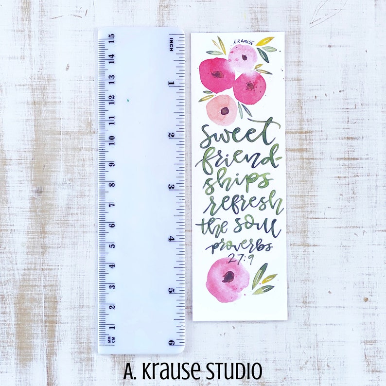 May include: A watercolor bookmark with pink floral accents and the text "Sweet friendships refresh the soul Proverbs 27:9." The bookmark is approximately 6 inches long and features green and pink calligraphy. The artist's name, A. Krause Studio, is at the bottom.