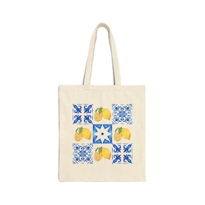 May include: A beige canvas tote bag featuring a grid pattern of nine squares. The design alternates between blue and white decorative tile motifs and illustrations of yellow lemons with green leaves, centered on the front of the bag.