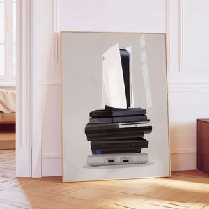 May include: A framed print featuring a stack of video game consoles, including a white and black PlayStation 5, and older models. The consoles are stacked on top of each other against a light gray background. The frame is gold.