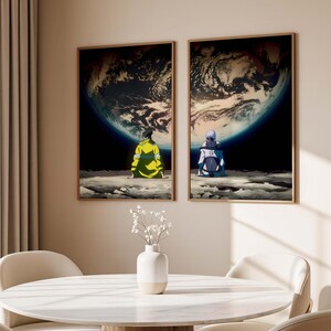 May include: Two framed art prints depict figures seated on a lunar surface, gazing at a large planet. One figure wears a yellow jacket, the other a blue and white outfit. The artwork features a dark, cosmic background with a detailed planet.