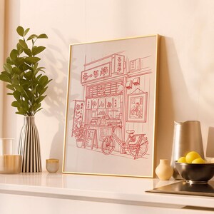 May include: A framed print featuring a red line drawing of a Japanese restaurant with a bicycle parked outside. The artwork includes Japanese text and a detailed depiction of the shop's facade, with hanging lanterns and signage.